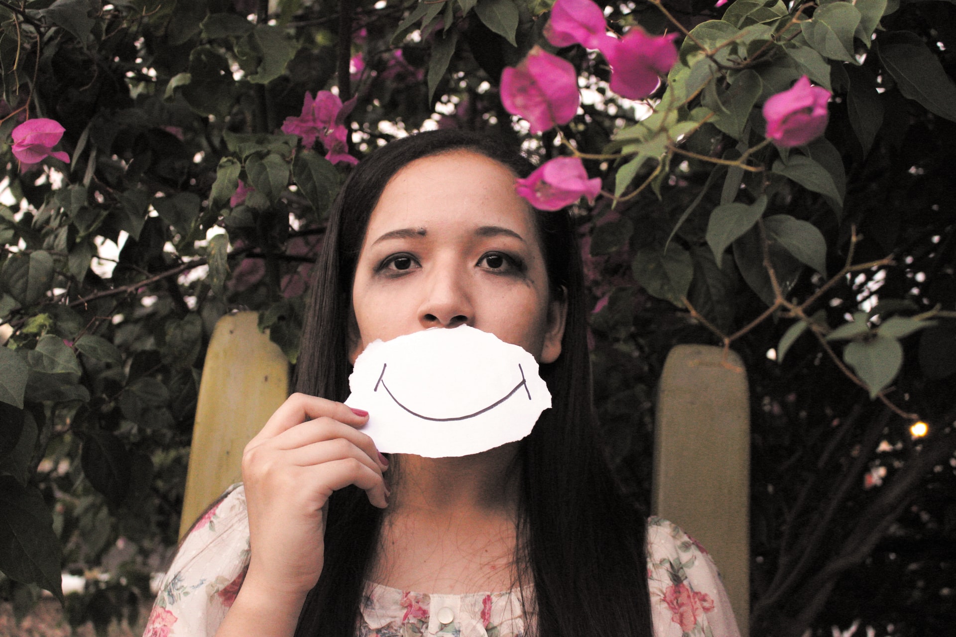 A girl holding a smiling face in front of her own face to mask her pain from self-harm