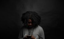 An African American female teen looking at her phone after she has been cyberbullied. Represents the need for teen therapy in Katy, TX 77494