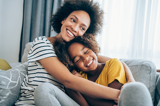 Lovely mother embracing her cute daughter on the sofa at home, How to Motivate Kids in a Healthy Way blog, counseling center at cinco ranch, counseling in katy texas, richmond texas